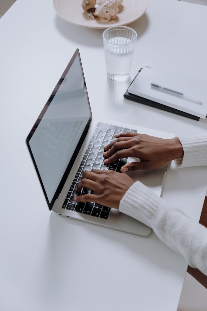 discover A woman typing on a laptop at a minimalist, modern home office desk, showcasing productivity.