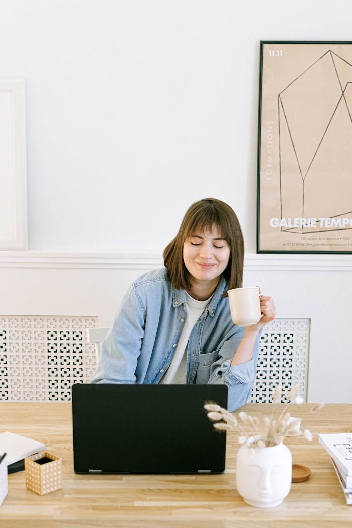 about-us Woman in a home office setting, smiling with a coffee cup near a laptop.